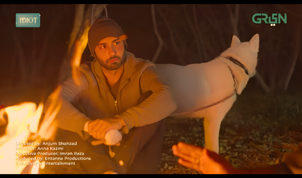 In the song of the Idiot drama, Ahmad Ali Akbar is sitting near a fire and a dog is standing near him
